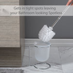 Toilet brush being held above a frosted holder on a chrome stand placed on a bathroom floor near a cabinet