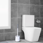 Toilet brush and holder placed on a tiled bathroom floor next to a modern white toilet