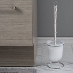 Toilet brush in frosted holder on chrome stand positioned on a marble-look floor beside a cabinet in a bathroom scene