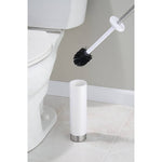 Toilet brush being lifted above a white cylindrical holder beside a toilet with stainless handle