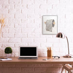 Lifestyle scene showing framed designer toilet-paper roll artwork hung above a desk with laptop, lamp and glasses.