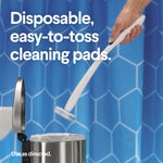 Hand holding a white ToiletWand over a trash can demonstrating disposable, easy-to-toss cleaning pads beside a toilet and shower curtain