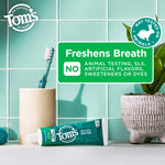 Tom's toothpaste tube on a bathroom counter with toothbrush, plant and a badge stating no animal testing and freshness benefits