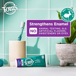 Tom's of Maine toothpaste tube lying on a tiled bathroom counter with toothbrush and badge stating no animal testing and enamel strengthening callout.