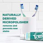 Toothpaste tube labeled Whiten+ Coconut Oil Gentle Mint partially visible on a bathroom counter with toothbrushes and claim about naturally derived micropolisher