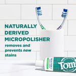 Toothpaste tube lying on counter next to cup with two toothbrushes and text about naturally derived micro-polisher