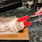 Hand using red silicone tongs to place seasoned chicken inside a clear vacuum sealer bag on a wooden board