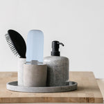 Light blue toothbrush case standing inside a concrete cup on a tray next to a hairbrush and soap dispenser