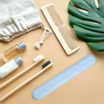 Single light blue speckled toothbrush travel case styled with toothbrushes comb and toiletry items on a tan background