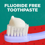 Close-up of a toothbrush head with a dollop of white toothpaste and bold text reading “FLUORIDE FREE TOOTHPASTE” above.