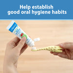 Hands applying toothpaste from a Dr. Brown’s tube onto the bristles of a giraffe-pattern infant toothbrush.
