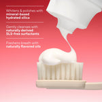 Close-up of toothpaste being squeezed onto a toothbrush head with product benefit text on a pink gradient background
