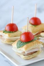 Appetizer bites with cherry tomato halves and basil secured by wooden toothpicks on a plate