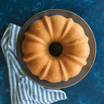 Top-down view of a baked bundt cake on a dark plate with a striped kitchen towel on a blue textured surface.