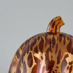 Top-detail of a tortoiseshell patterned pumpkin-shaped fragrance warmer showing its stem and curved surface