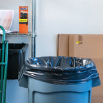 Black trash bag lining a gray utility trash can in a garage scene with a Hefty product box on a metal shelf