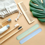 Speckled green and blue toothbrush travel cases styled with bamboo toothbrushes, small bottles and a leaf on a beige surface.