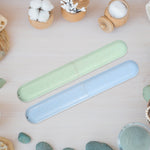 Speckled green and blue toothbrush travel cases arranged on a light wood surface among cotton, jars, and spa-style accessories.