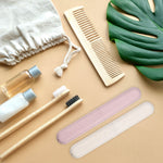Two toothbrush travel cases laid beside bamboo toothbrushes, comb, and toiletry bottles in a travel lifestyle flatlay.