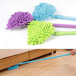 Close arrangement of three triangular microfiber mop heads and handles in blue, purple, and green with a person using a long handle to reach under furniture.