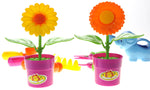 Two pink pots with plastic sunflowers in front and a blue elephant watering can and tools blurred in the background.