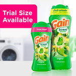 Two sizes of Gain scent booster bottles on a counter with a pink panel stating 'Trial Size Available' and a blurred washer in background