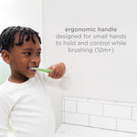 Young child brushing with a green toddler toothbrush next to overlay text about an ergonomic handle designed for small hands (12m+).