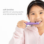 Child holding and brushing with a purple toddler toothbrush, with overlay text reading soft bristles gentle on young gums and developing teeth.