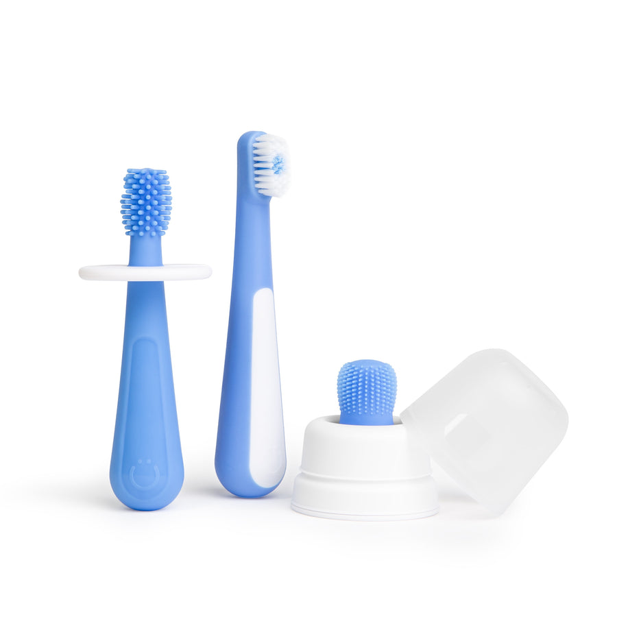 Three blue toddler toothbrush training pieces including silicone finger brush, soft-bristled brush and white cover/base on white