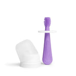 Ubbi purple silicone training toothbrush shown with a white safety shield and a translucent cap beside it on a white background.