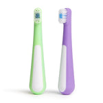 Two Ubbi toddler toothbrushes standing upright on white background, one purple and one green with white grip panels.