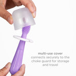 Hands placing a translucent multi-use cover over a purple silicone toddler toothbrush shown on white