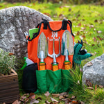 Ukoke orange tool apron propped outdoors with metal trowel, fork and spray bottle tucked into pockets by rocks and grass.