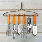 Row of six Ukoke orange-handled garden tools hung from a rustic metal rack against pale wooden boards.