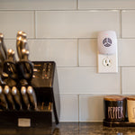 White ultrasonic pest repeller plugged into a kitchen outlet beside knife block and labeled spice canisters on counter