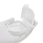 Open clear plastic retainer case held in a gloved hand, showing interior cavity and hinge with a white background