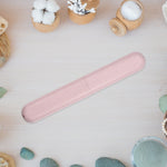 Pink speckled toothbrush travel case placed on a light wood surface surrounded by spa-style items