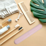 Pink travel toothbrush case shown with bamboo toothbrushes, comb and toiletry items in a lifestyle flatlay