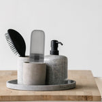 Gray toothbrush travel case placed upright in a stone holder next to a pump dispenser and hairbrush