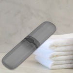 Gray toothbrush travel case with black latch placed on a countertop beside folded white towels