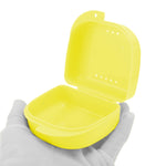 Open yellow plastic retainer case held in a gloved hand, showing interior and ventilation holes.