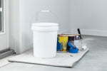 White utility bucket with lid placed on drop cloth beside paint cans, roller, and painter's tools in a workspace