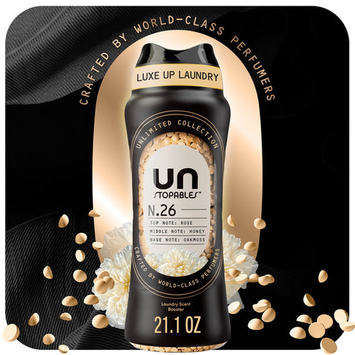 Black bottle of Unstopables N.26 scent booster surrounded by scattered beige beads and white flowers