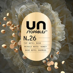 Gold oval label reading UNSTOPABLES N.26 with listed top, middle and base notes over a soft floral background