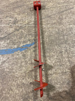 Red metal earth anchor with spiral auger blades and square top lying on a workshop floor surface.