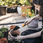 Person using a Fiskars ergonomic trowel to transfer soil into a terracotta pot on a sunlit deck with potted plants