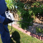 Person using a Chapin pump sprayer to apply a spray along a garden bed, showing wand, hose and spray stream