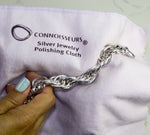 Hand using a Connoisseurs silver jewelry polishing cloth to polish a chunky silver chain bracelet