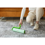 Person kneeling on floor using a green Evercare lint roller to pick up pet hair and debris from a rug