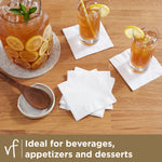 Lifestyle image of Vanity Fair white beverage napkins on a wood table next to glasses and a pitcher with lemon slices